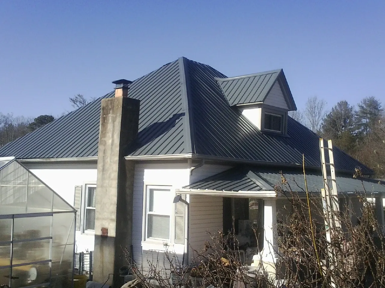 Dark blue standing seam metal roof on a white farmhouse with dormer — Slate & Tile Roof Repair by Roofing Brothers in Dry Fork