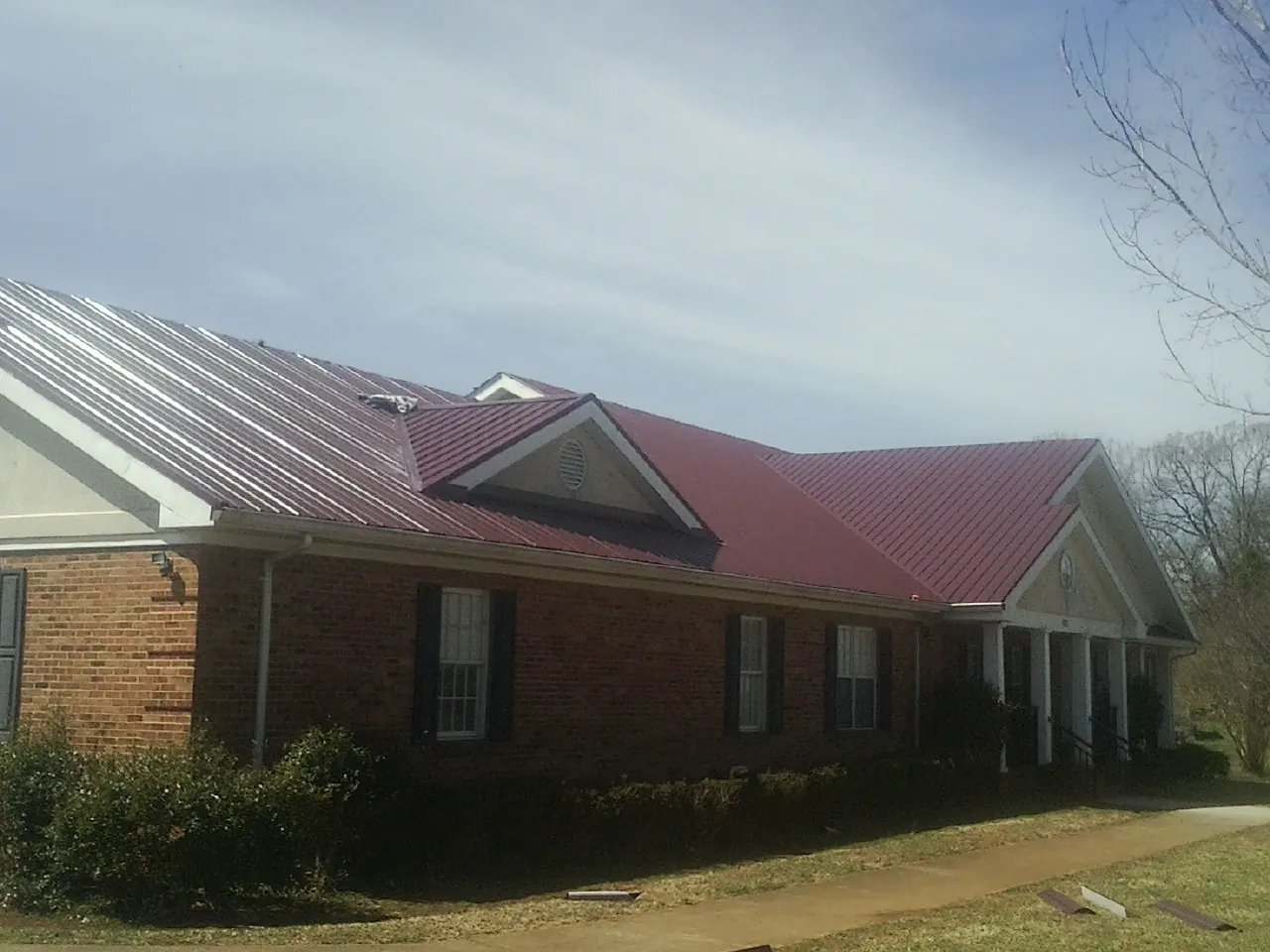 Red metal roof with gabled entries on a long brick building, from a Hail Damage Roof Repair job in Dry Fork