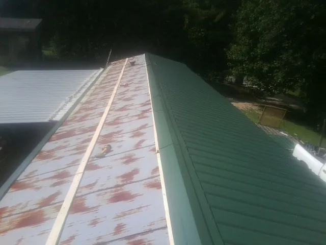 Old rusted panels beside newly installed green metal roofing — Wind Damage Roof Repair by Roofing Brothers in Dry Fork
