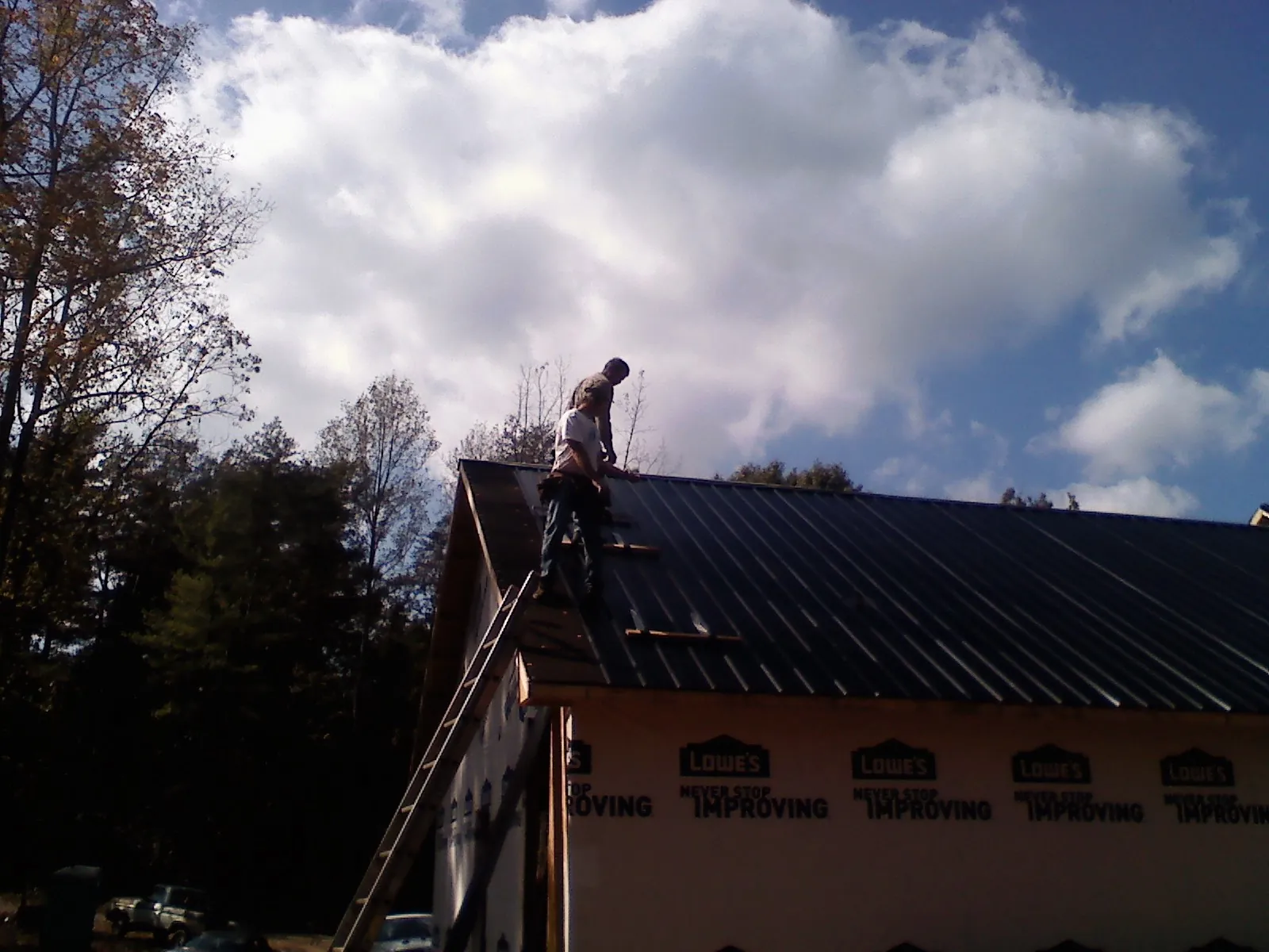 Roofer fastening dark metal panels high against a cloudy sky, from a Roof Inspection job in Dry Fork