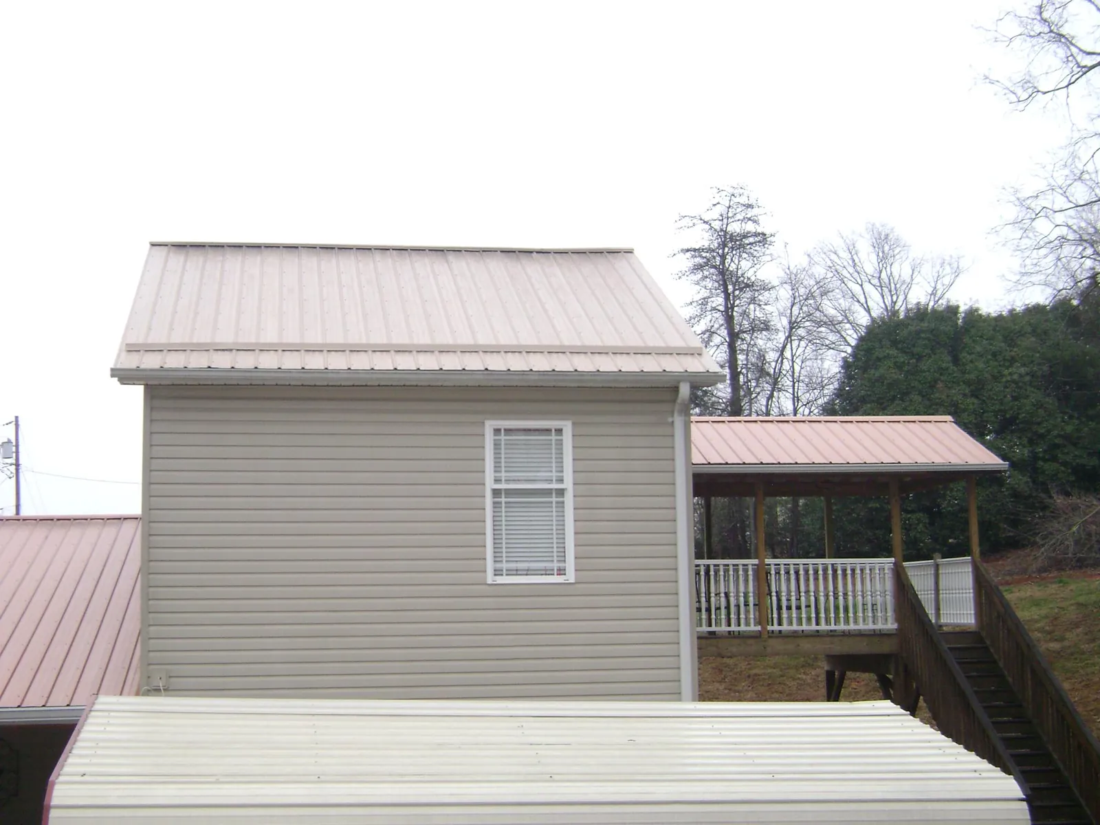 Tan metal roofs on a two story addition and attached porch, from a Roof Replacement job in Dry Fork
